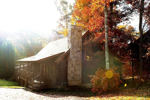 A rustic log cabin with a stone chimney, surrounded by autumn foliage.