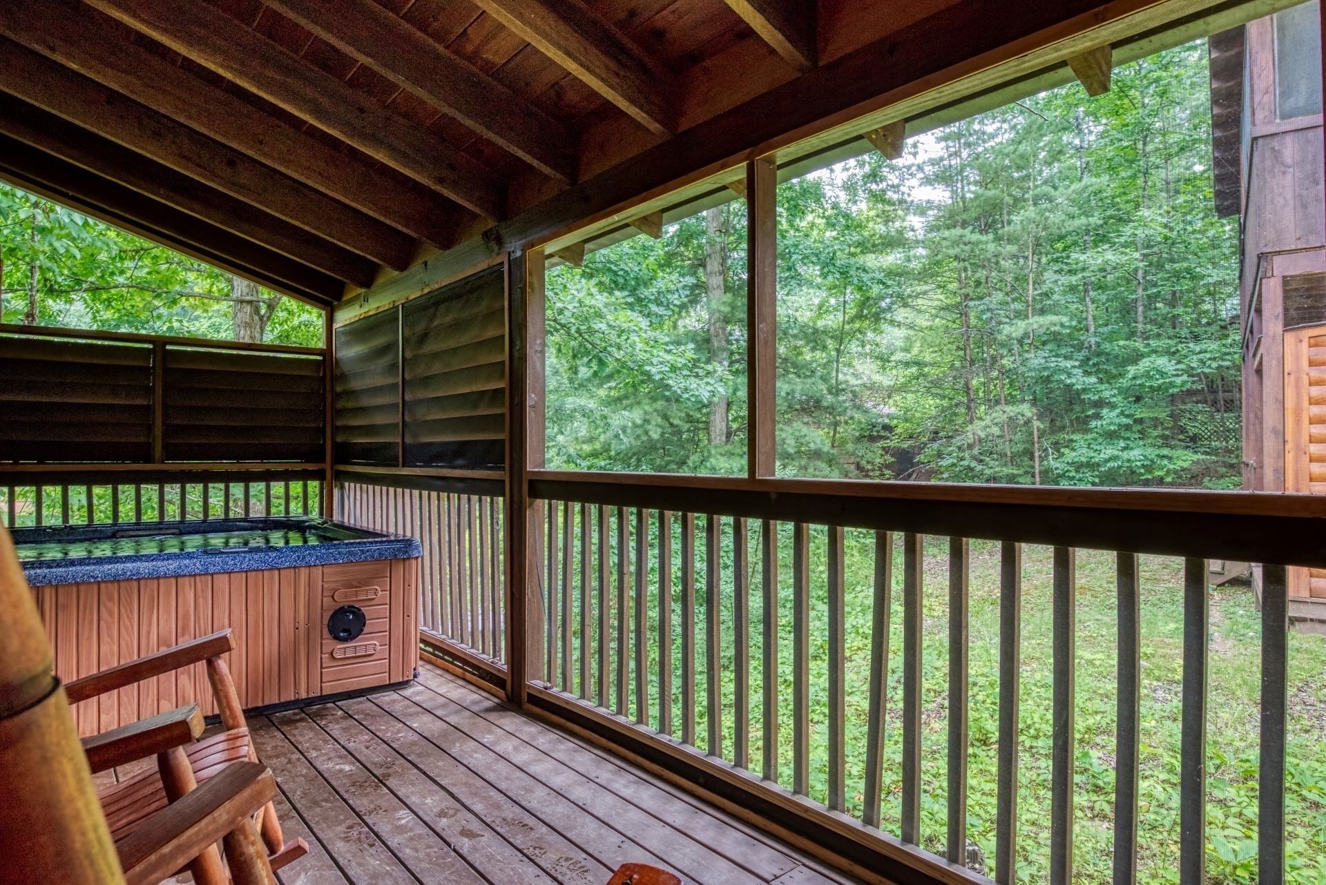 Een houten terras met een jacuzzi, houten banken en uitzicht op een bos.