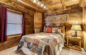 Una acogedora habitación de cabaña de madera con una cama grande, una mesita de noche con lámpara y un adorno decorativo sobre la cama.