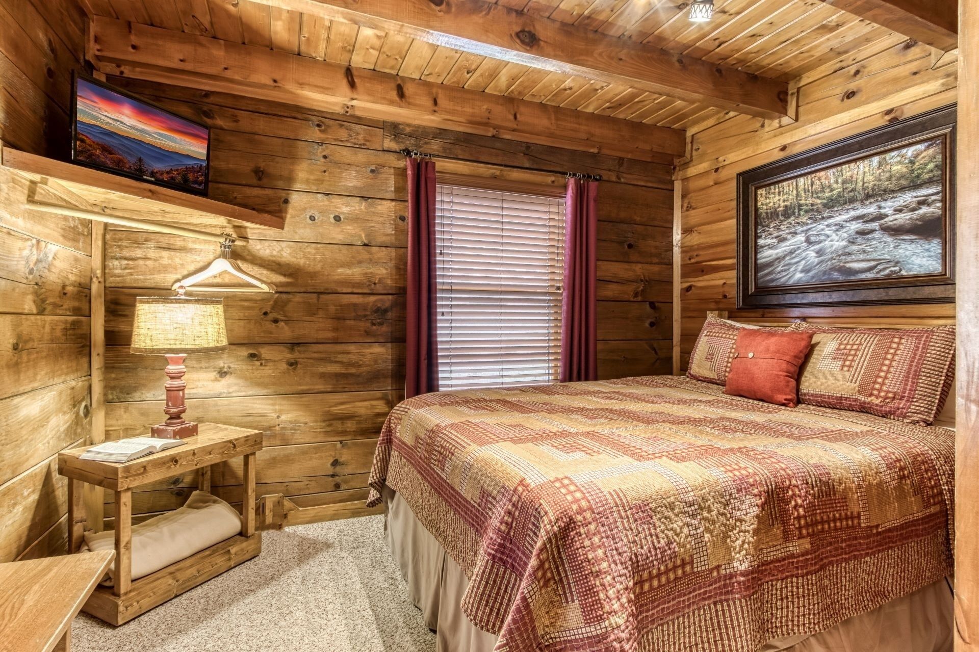 A wooden cabin bedroom with a bed, a nightstand, a lamp, and a painting on the wall.