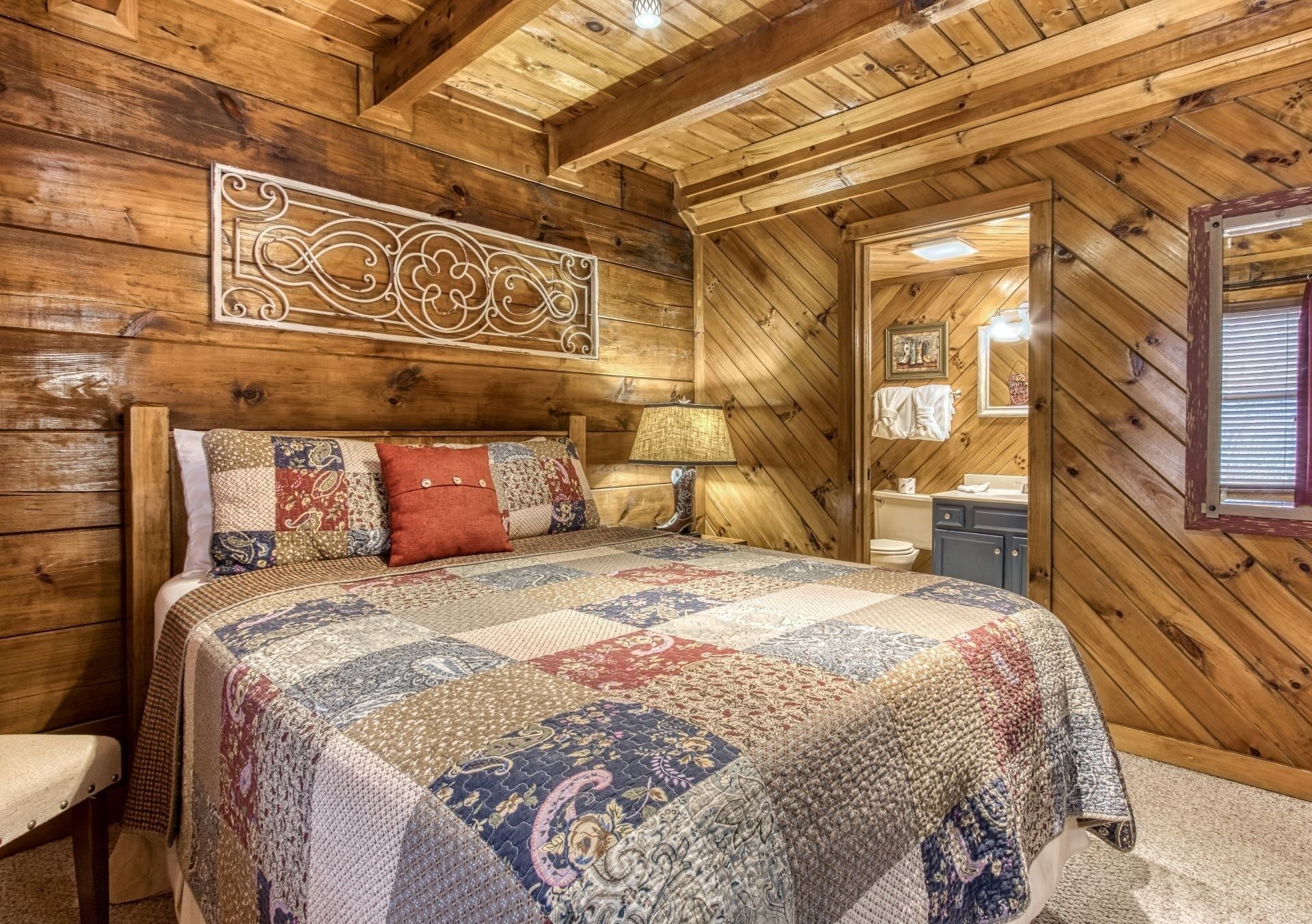 A cozy wooden cabin bedroom with a large bed, a decorative wall piece, and a view of the bathroom through an open door.