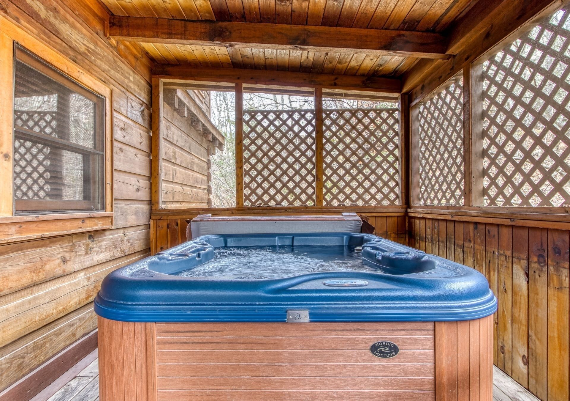 Ein Whirlpool in einer Holzhütte mit Gitterfenstern und Holzboden.