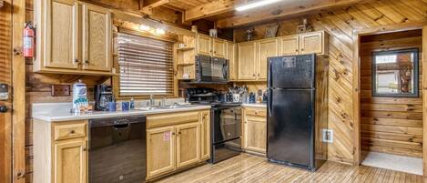 A wooden cabin interior with a kitchen featuring wooden cabinets, a stainless steel refrigerator, a microwave, and a stove.