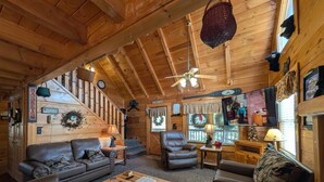 A cozy cabin interior with a wooden ceiling, a staircase, a fireplace, and a dining area. - ER245 - Almost Heaven Great Location - Close To Town! 3 Bedroom Cabin by RedAwning (Pigeon Forge)