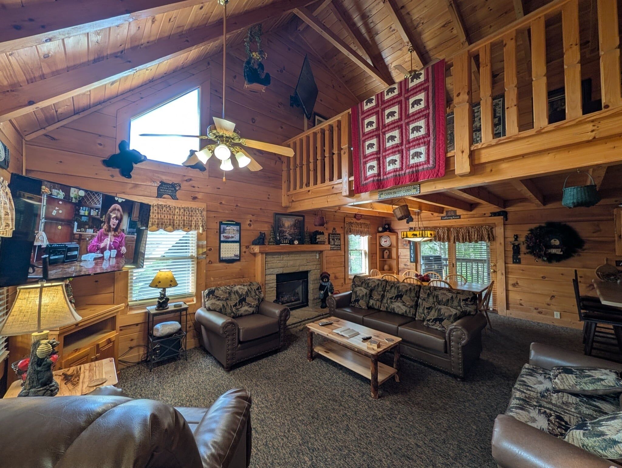 Ein gemütliches Blockhaus-Interieur mit Kamin, Holzmöbeln, einem Fernseher und einem Schlafbereich mit roter Steppdecke.