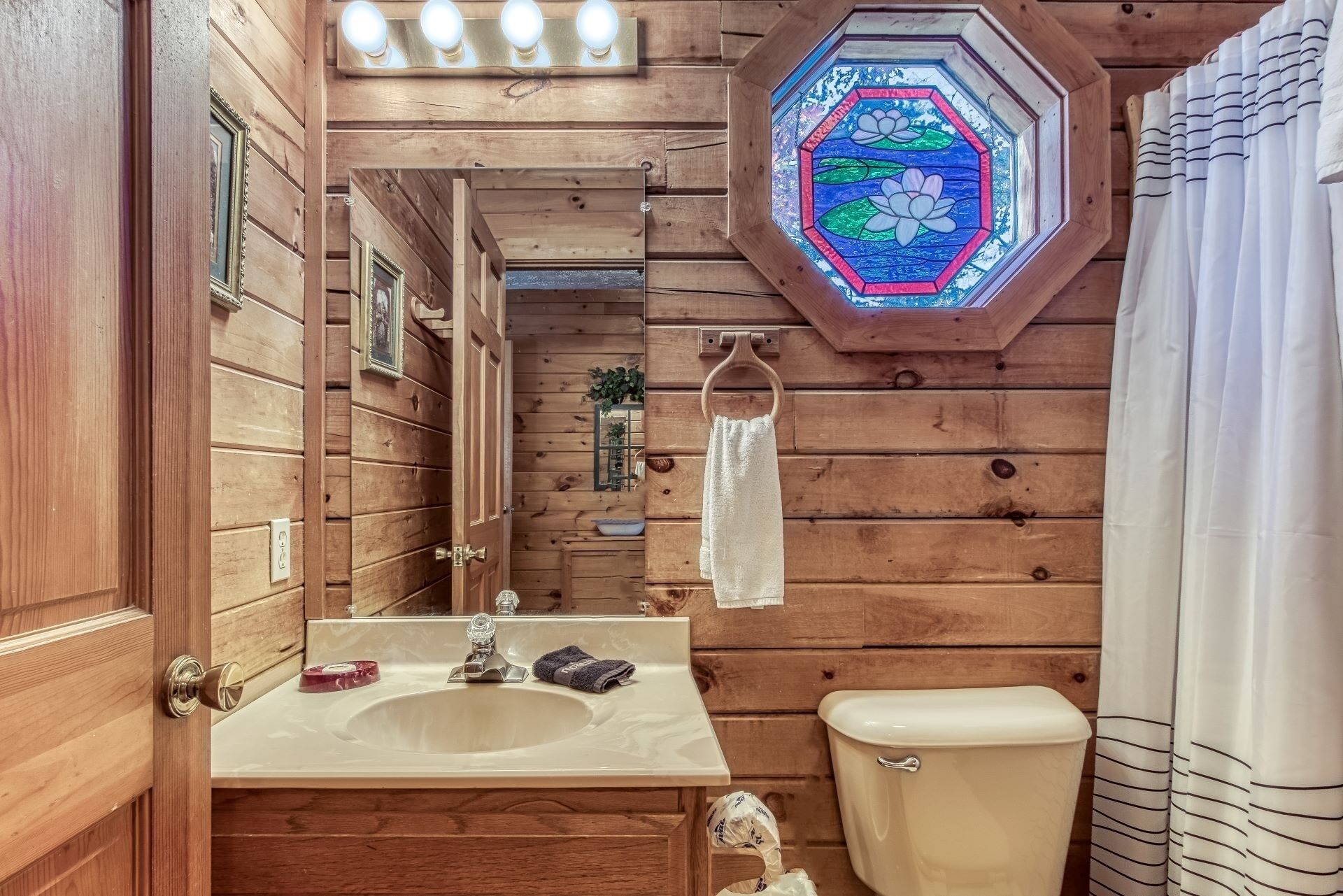 A wooden bathroom with a sink, mirror, towel rack, and a stained glass window.