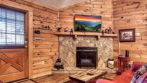 Un intérieur de chalet chaleureux avec une cheminée en pierre, des murs en bois, un téléviseur fixé au mur et un canapé en cuir rouge.