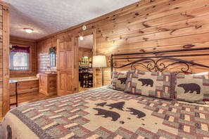 A cozy wooden cabin bedroom with a bed, a nightstand, a lamp, and a window with blinds. - Er102 - Barbara Great Location! Close To Town 2 Bedroom Cabin by RedAwning (Pigeon Forge)