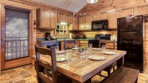 Une cuisine rustique aménagée dans une cabane en bois, avec une table à manger pour quatre personnes, des placards en bois, un four à micro-ondes et un réfrigérateur.