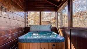 A wooden cabin with a hot tub in the center, surrounded by large windows offering a view of autumn trees. - Er84 - Serenity Summit - Great Location. Close To All The Action! 1 Bedroom Cabin by RedAwning (Pigeon Forge)