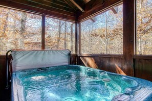 Un jacuzzi en una cabaña de madera con ventanas amplias que dan a un bosque.
