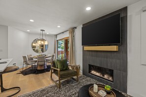 A modern living room with a fireplace, a dining area, and a TV mounted on the wall. - Snow Flower 044 2 Bedroom Condo by RedAwning (Park City)