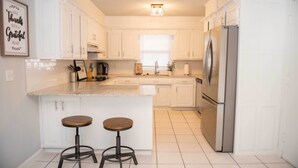Una cocina moderna con armarios blancos, un refrigerador de acero inoxidable y dos taburetes de madera.