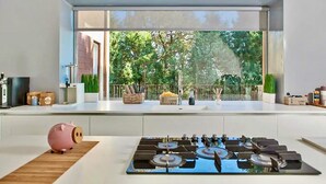 A modern kitchen with a gas stove, a pink piggy bank, and a large window overlooking a garden.