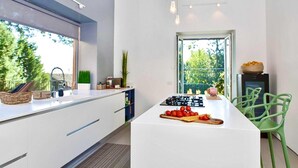 A modern kitchen with a central island, white cabinetry, and a view of greenery outside.