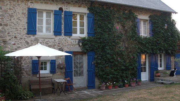 Un edificio in pietra con persiane blu, un ombrello bianco e piante in vaso.