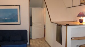 Un ambiente compatto con un divano blu scuro, una porta bianca, un angolo cottura con una lampada e un quadro appeso al muro.