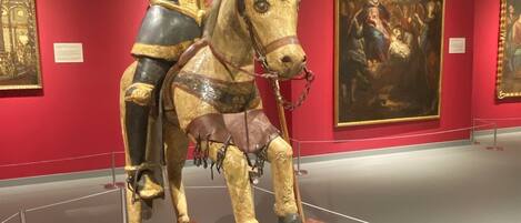 Une sculpture représentant Santiago Matamoros à cheval, exposée dans un musée aux murs rouges, avec des tableaux encadrés en arrière-plan.
