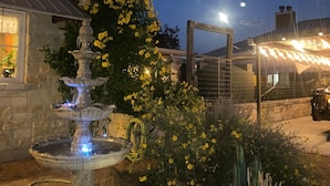 A stone building with a multi-tiered fountain in the foreground, surrounded by yellow flowering plants. - Happy Trails Cowboy Cabin HOT TUB POOL on 12 ac (Bandera)