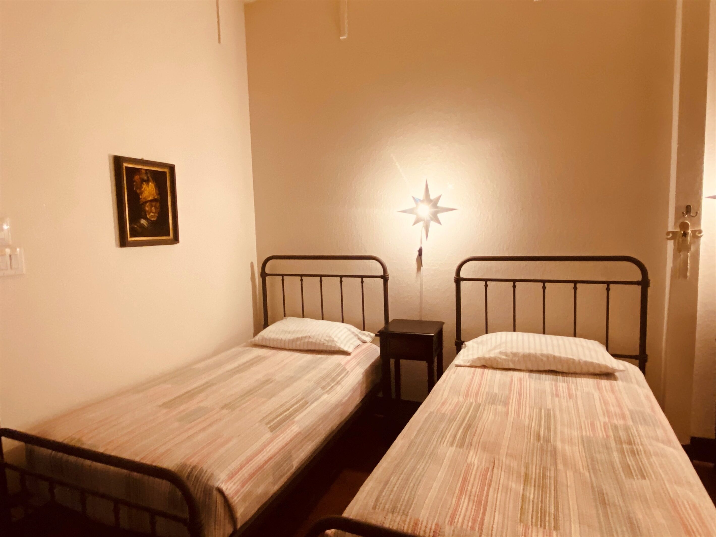 A room with two single beds, a nightstand, a star-shaped wall decoration, and a framed picture on the wall.