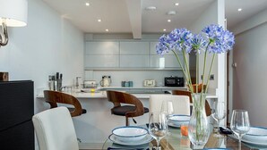 A modern kitchen with white cabinets, a dining area with a table set for two, and a vase with blue flowers.