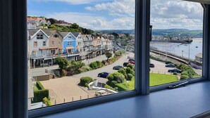 A view from a window overlooking a coastal street with houses, parked cars, and a body of water.
