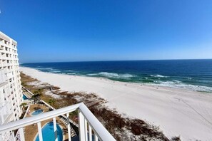 Vista a la playa desde un balcón con piscina y sillones de sol.