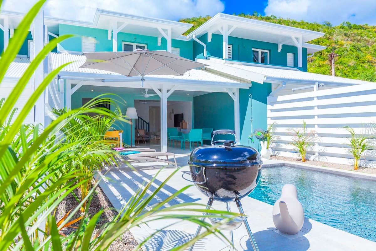 A poolside area with a barbecue grill, outdoor seating, and a view of a house with a pool.