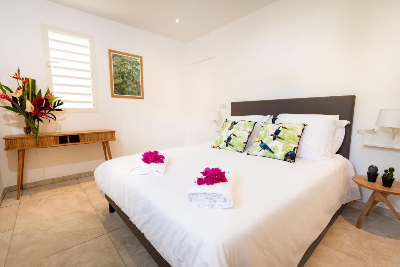 A neatly made bed with white linens and decorative pillows, a bedside table with a lamp, and a small potted plant.