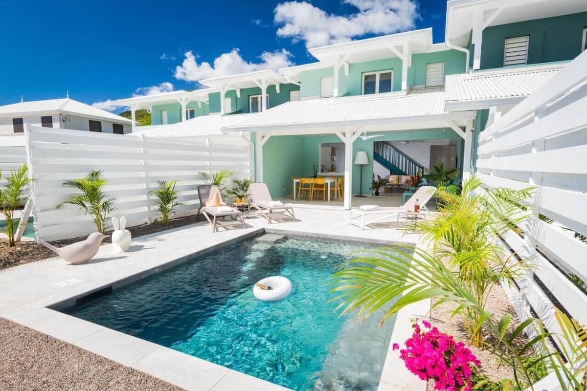 A pool area with a clear blue pool, lounge chairs, and a dining area with a table and chairs.