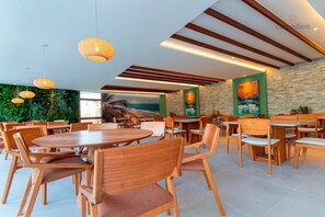 A spacious dining area with wooden tables and chairs, a green wall with a mural, and pendant lighting.