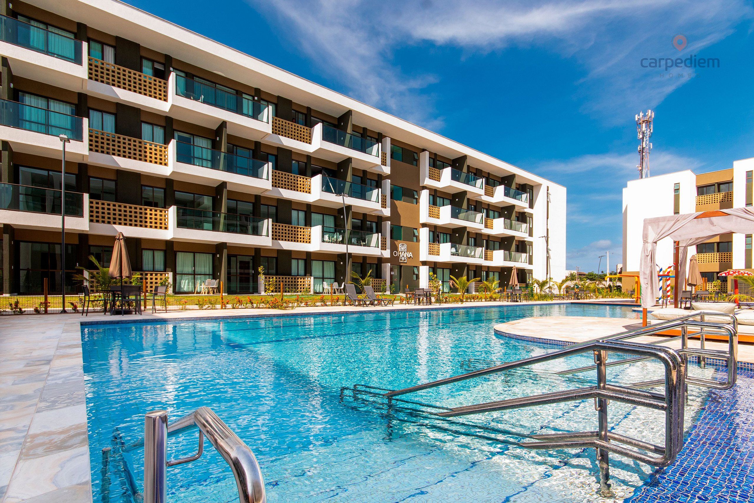 A modern hotel with a swimming pool, multiple balconies, and outdoor seating areas.