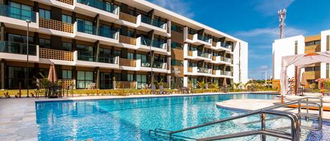 A modern hotel with a swimming pool, multiple balconies, and outdoor seating areas.