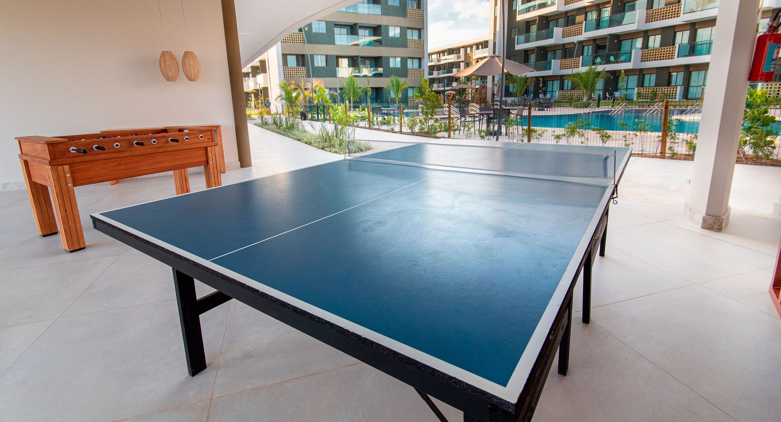 A ping pong table in an outdoor area with a pool and a building in the background.