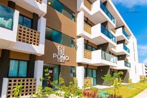 A modern hotel with multiple balconies, a prominent logo, and a well-maintained garden area. - Mana Beach Experience B16 - Carpediem (Ipojuca)