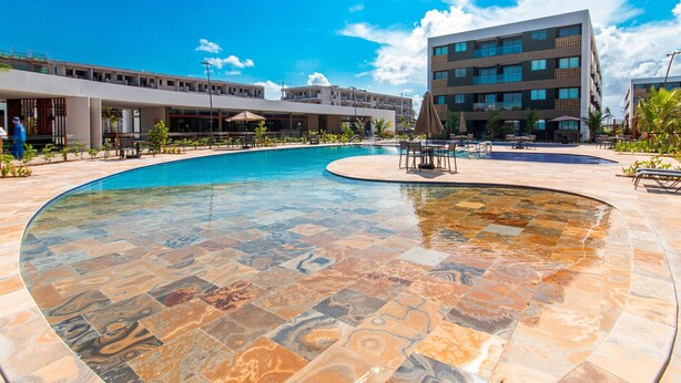 Una piscina con un design delle piastrelle unico, circondata da posti a sedere all'aperto e un edificio moderno sullo sfondo.