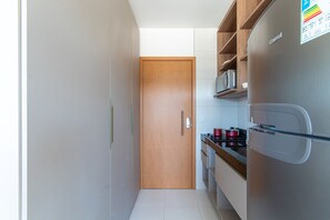 A compact kitchen with a wooden door, stainless steel appliances, and a microwave shelf. - Mana Beach Experience B16 - Carpediem (Ipojuca)