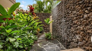 Un chemin de pierres menant à un élément décoratif aquatique, bordé d’un mur de pierres et agrémenté d’une végétation tropicale luxuriante.