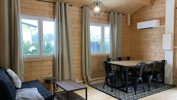 Una habitación acogedora con techo de madera, un sofá con manta, una mesa de comedor con sillas y un tapete estampado.
