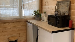 Cocina compacta con paredes de madera, un refrigerador pequeño, un microondas y una cafetera.