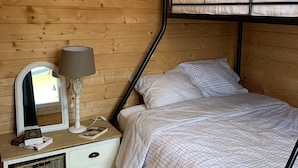 Un dormitorio de cabaña de madera con una cama litera, una mesita de noche con lámpara, un espejo y un pequeño aparador.
