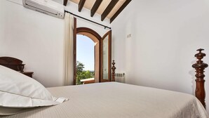 A bedroom with a large bed, an air conditioning unit, a wooden headboard, and a view through an arched doorway. - Villa in Búger perfect for children with swimming pool, paddle court and large garden (Búger)