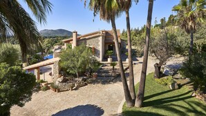 A stone building with a patio area, surrounded by palm trees and potted plants. - Villa in Búger perfect for children with swimming pool, paddle court and large garden (Búger)
