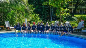 Un groupe de personnes est assis au bord d’une piscine, avec un jardin tropical en arrière-plan.