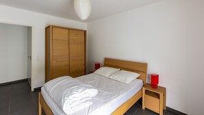 Ein ordentlich bezogenes Bett mit weißen Leinen, einem Holzkopfstück und zwei Nachttischen mit roten Lampen.