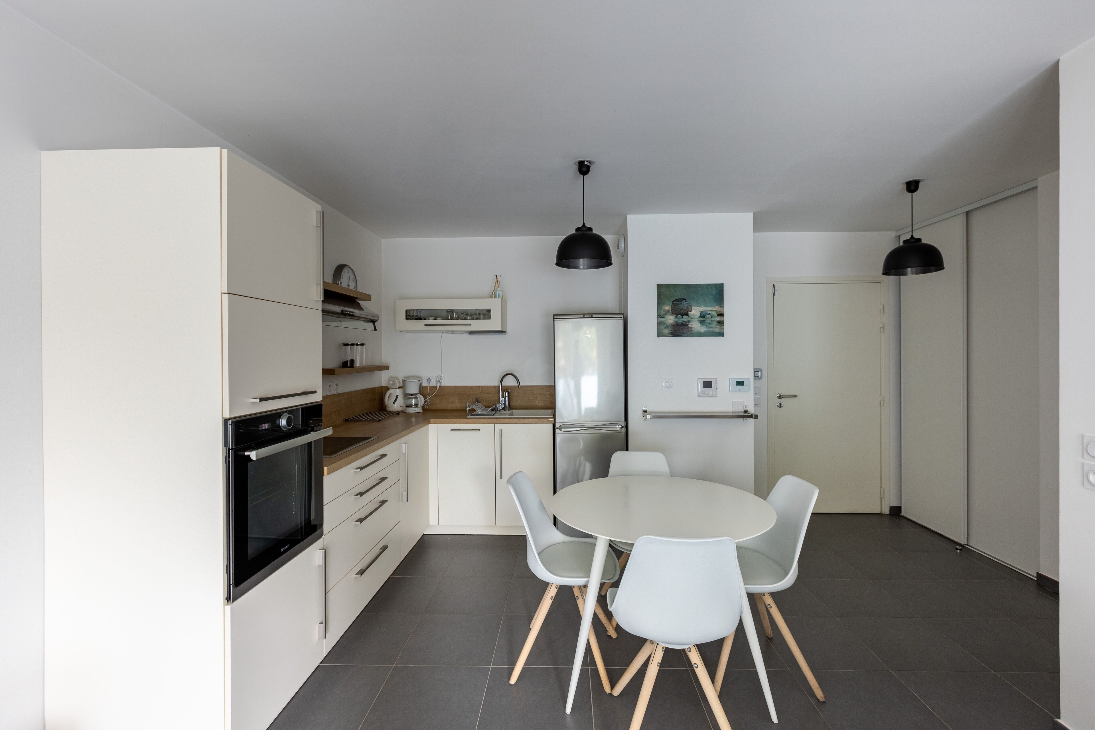 A modern kitchen with white cabinetry, a dining table with chairs, and two pendant lights.
