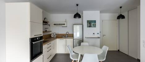 A modern kitchen with white cabinetry, a dining table with chairs, and two pendant lights.