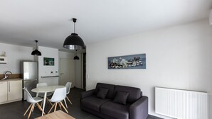 Ein modernes Wohnzimmer mit einem grauen Sofa, einem Esstisch mit Stühlen, einem Holztisch und einem weißen Heizkörper.