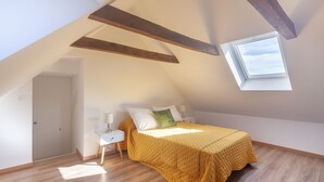Ein Schlafzimmer mit Schrägdecke, einem Oberlicht, einem Bett mit gelber Bettdecke und Holzbalken.