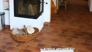 A room with a fireplace, a wooden bench, a tiled floor, and a basket of firewood. - Vacation home Vogelbeere -Idyllic vacation home with half-timbered house between Fleesensee and Golf (Göhren-Lebbin)